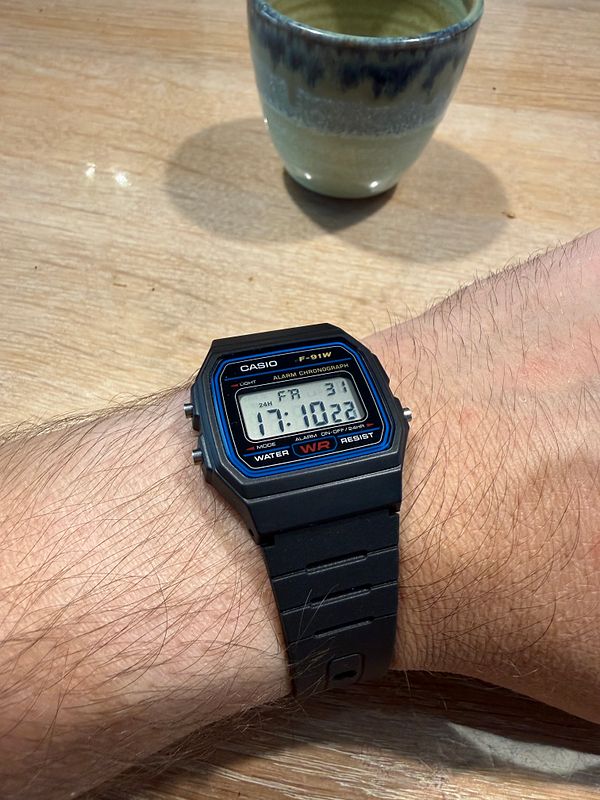 Photo of a wrist wearing a black wristwatch with a round black dial and a silver bezel.