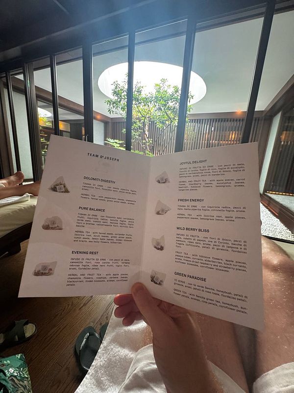 A person is holding a tea menu from a wellness spa, showcasing various herbal and fruit tea options.