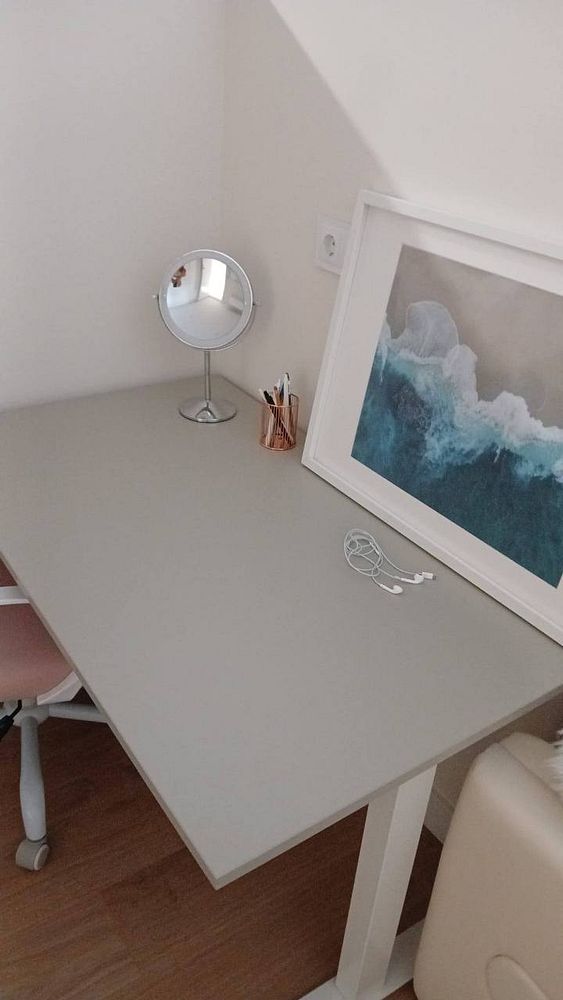 A cozy, minimalist coworking space with carefully arranged plants, a laptop on a desk, and a wall adorned with art prints and paper decorations.