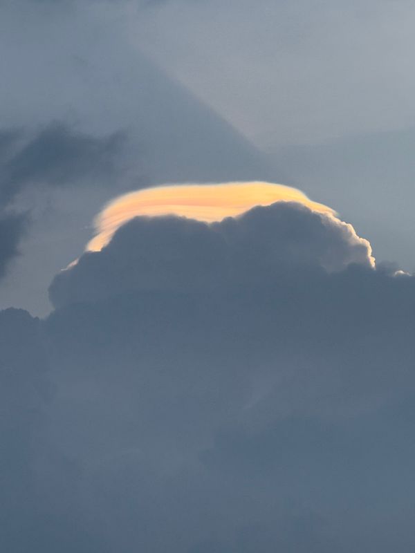A striking cloud formation with a golden edge against a backdrop of gray clouds.