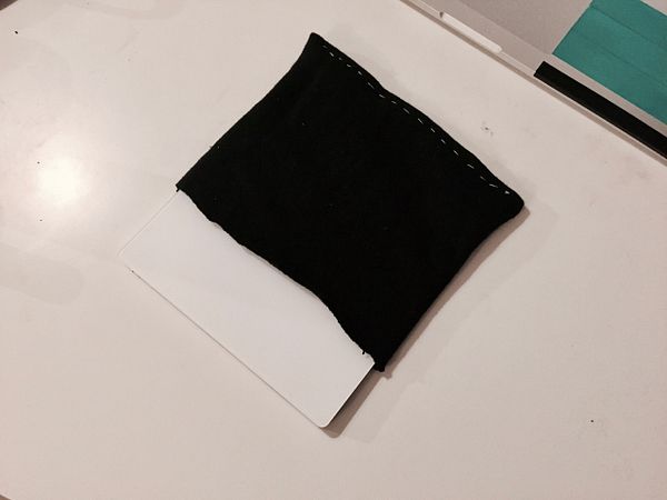 The image shows a trackpad being partially inserted into a black fabric sleeve on a table.