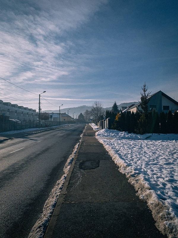 A serene winter morning scene featuring a long, empty road lined with snow and houses.