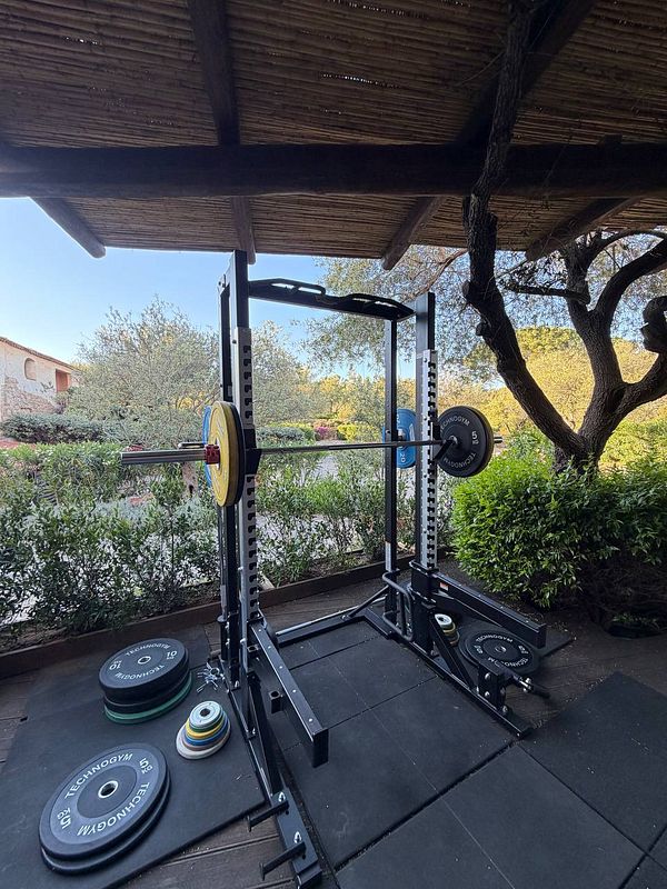 Outdoor gym equipment on a stone terrace overlooking turquoise sea waters with a sunny sky.