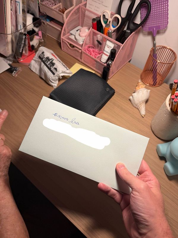 A hand is handing over a legal letter on top of a blue and white pillow with floral patterns.
