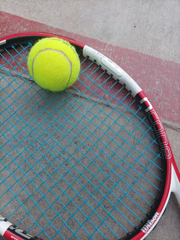 A tennis racket with a bright yellow tennis ball resting on its strings.