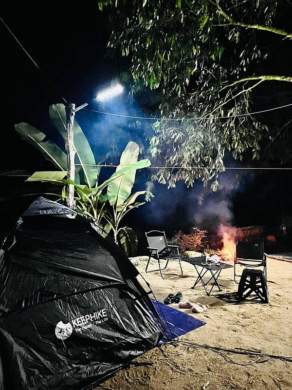 A nighttime camping scene featuring a tent, chairs, and a campfire.