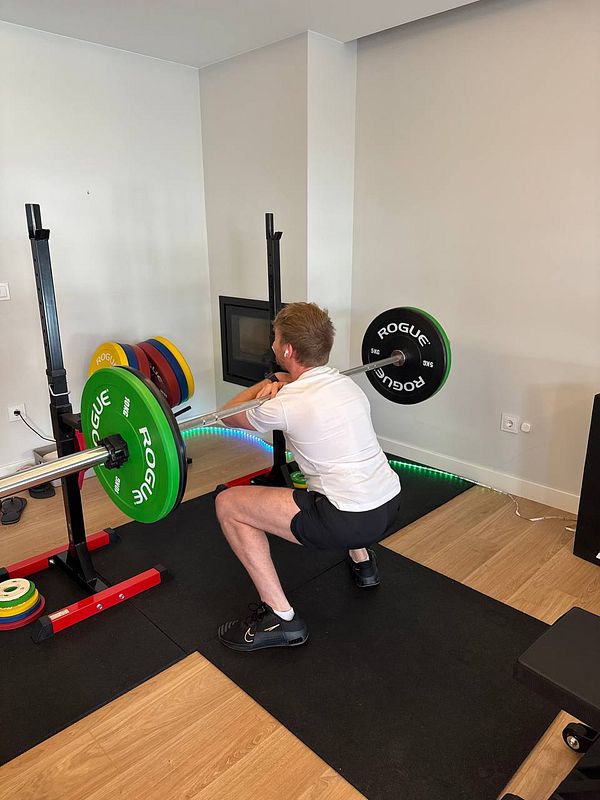 A person is performing a squat with a barbell in a home gym setting.