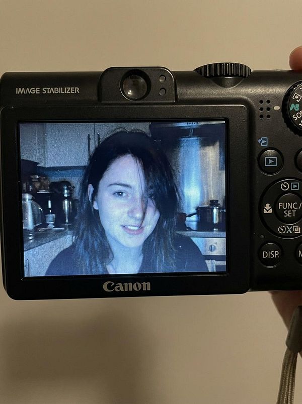 A person is smiling while being photographed on a Canon camera, with a kitchen background visible.
