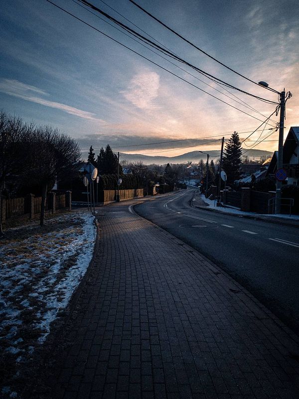 A serene morning scene of a winding road surrounded by trees and houses under a cloudy sky.