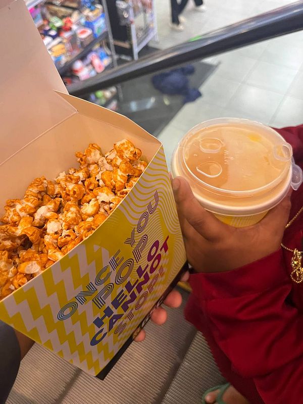 A person is holding a box of popcorn and a drink in a busy environment.