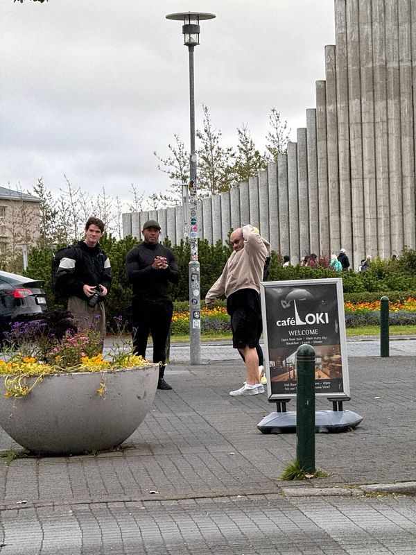 Three individuals are gathered outside a café, discussing their experiences with fermented shark.