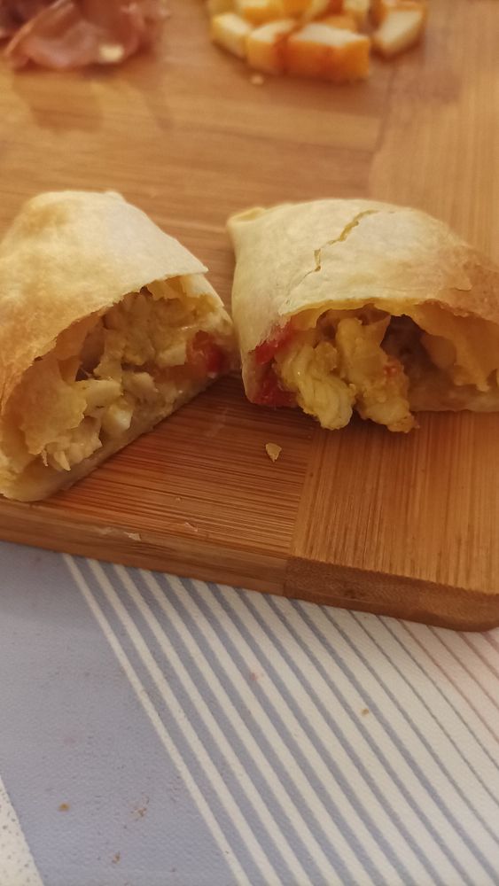 Two chicken empanadas are displayed on a wooden cutting board, one cut in half to reveal its filling.