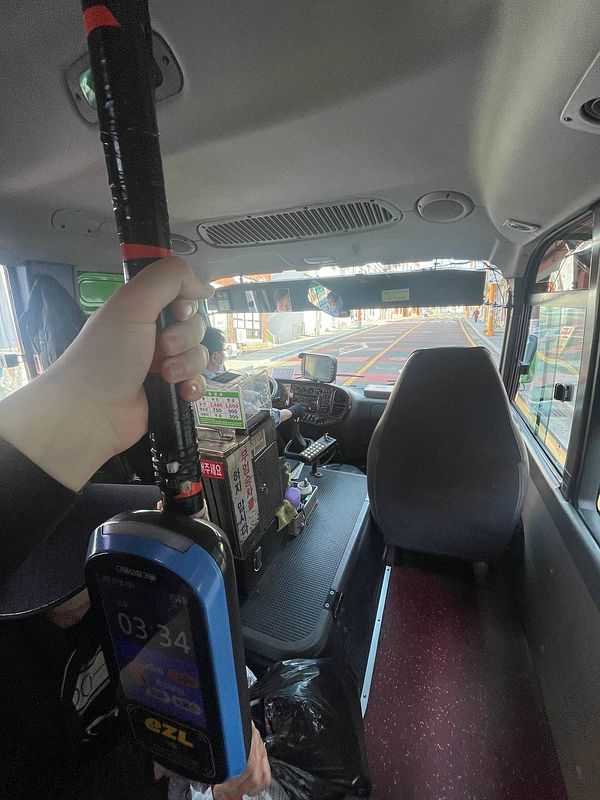 The image captures the interior of a small bus designed for narrow mountain roads, showcasing a handheld device and the bus driver's area.
