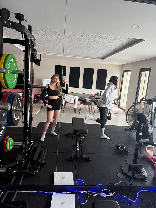 A person lifting a heavy black barbell in a gym setting with dumbbells in the background.