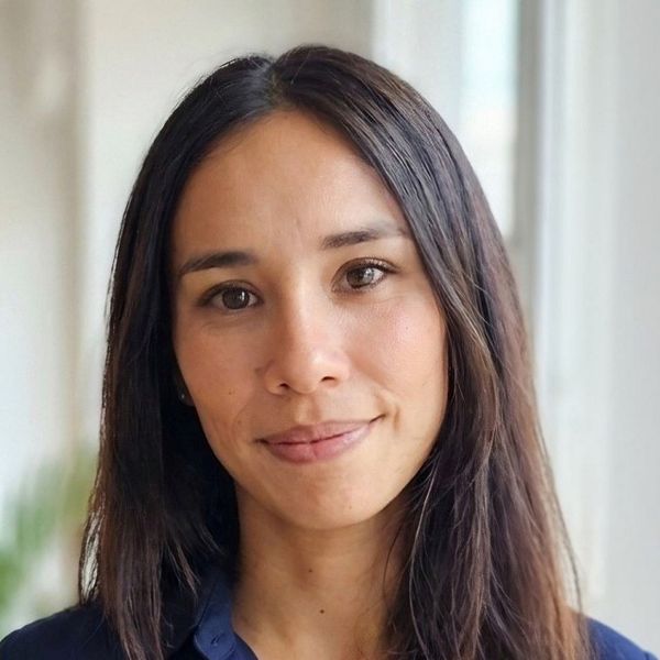 Close-up portrait of a young woman with long dark hair, bright eyes, and natural makeup, set against a neutral floral background.