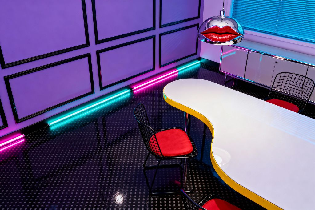 A Pop Art dining room with lavender wall panels trimmed in black, neon cyan and magenta tube lights, a sculptural white dining table with a yellow edge and chrome legs, black wire chairs with red velvet cushions, a chrome dome pendant featuring red lips, a glossy black floor with white polka dots, and a white lacquer sideboard beneath blue window blinds.