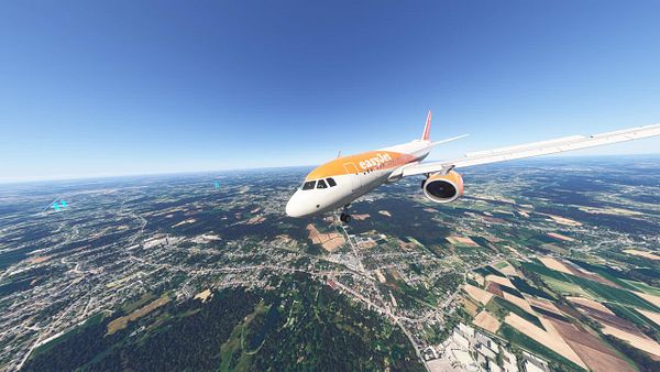 An aircraft in flight over a landscape featuring fields and urban areas.