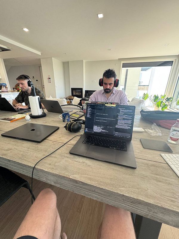 A coworking space setup with two individuals working on laptops at a wooden table.