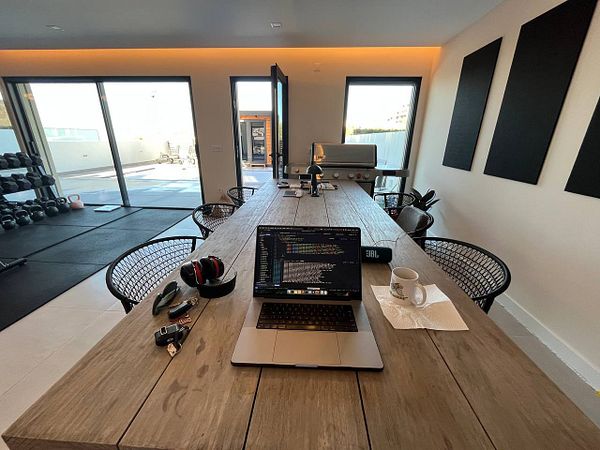 A modern coworking space featuring a large wooden table with a laptop and various personal items.