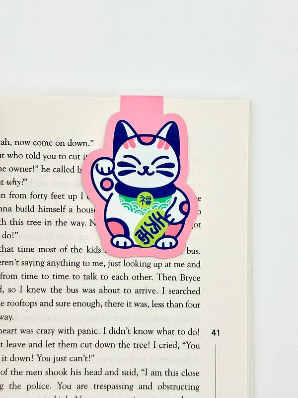 A colorful magnetic bookmark featuring a cartoon cat design is placed on an open book page.