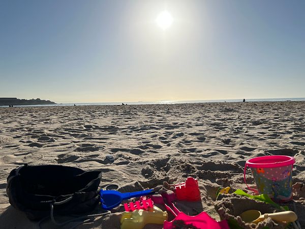 A sunny beach scene with children's sand toys in the foreground.