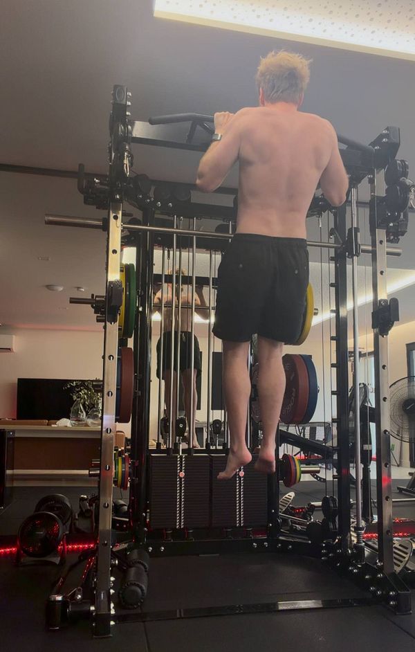 Photo of a man doing a pull-up on a bar outside near greenery.
