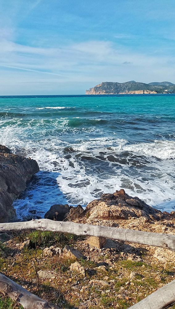A woman and a man walk hand in hand on a gravel path beside a field under a partly cloudy blue sky.