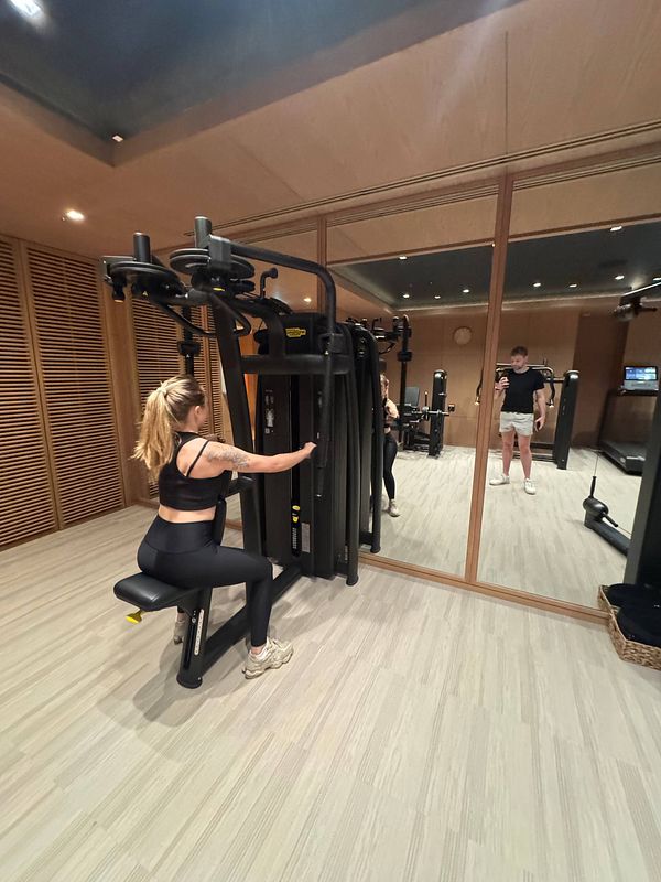 A woman is exercising on a gym machine while a man stands nearby.