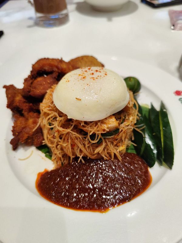 A beautifully plated brunch dish featuring noodles, fried chicken, and a soft bun.