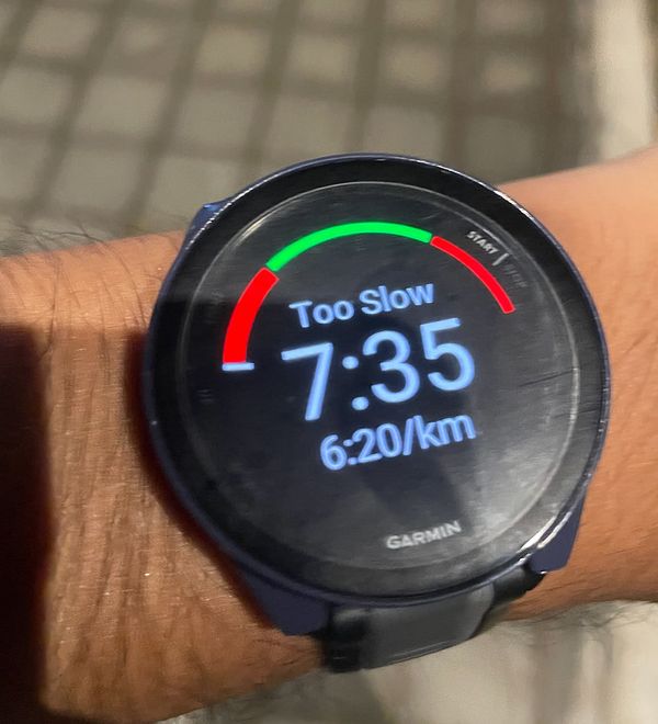 A Garmin smartwatch displays a running pace alert indicating the user is too slow.