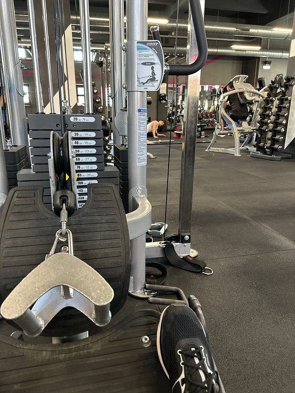 A gym setting featuring a cable machine with weights and a person exercising in the background.