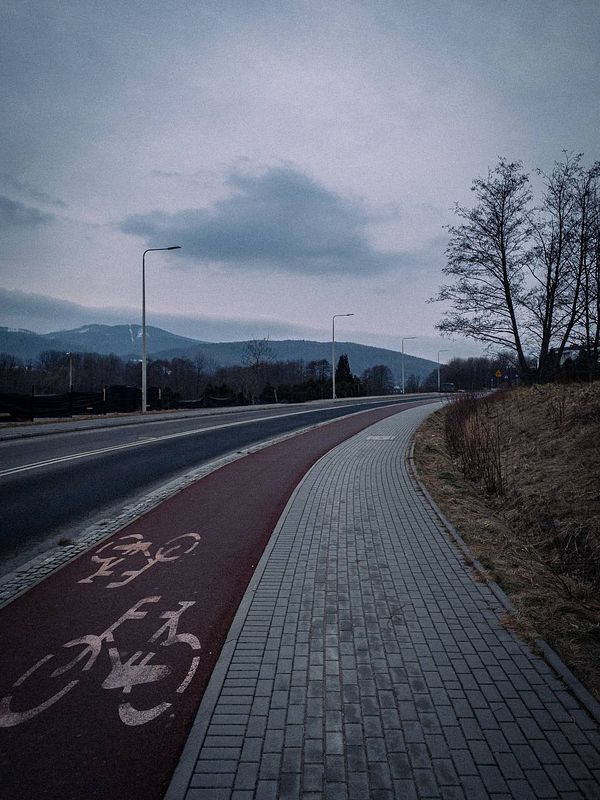 A serene morning scene featuring a winding path alongside a road, with mountains in the background under a cloudy sky.