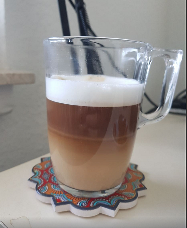 A cup of cappuccino on a wooden surface next to a white napkin and a partially visible laptop keyboard.