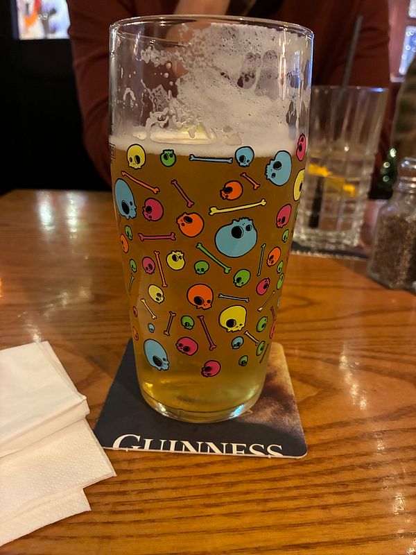 A colorful pint glass filled with beer sits on a wooden table.