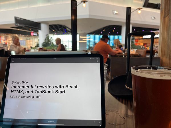 A tablet displays a presentation about web development while a beer sits on a table in an airport setting.