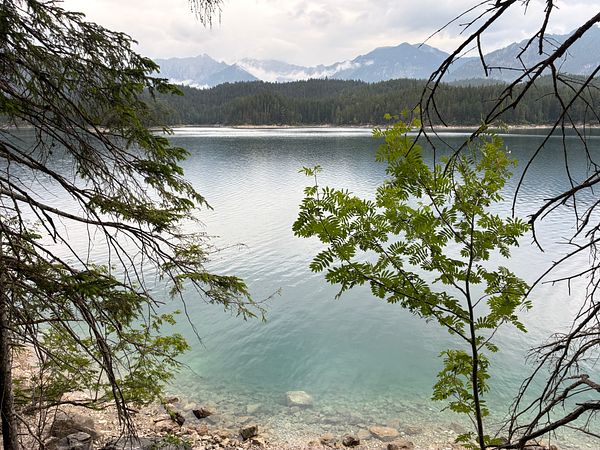 A serene lake with a wooden dock extending into the water, surrounded by forested hills under a cloudy sky.