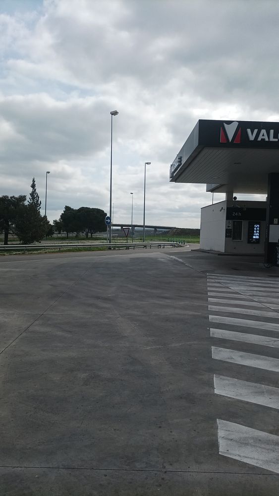 Photo of a roadside green sign indicating the halfway point to Barcelona, with a motorcycle and scenic landscape in the background.