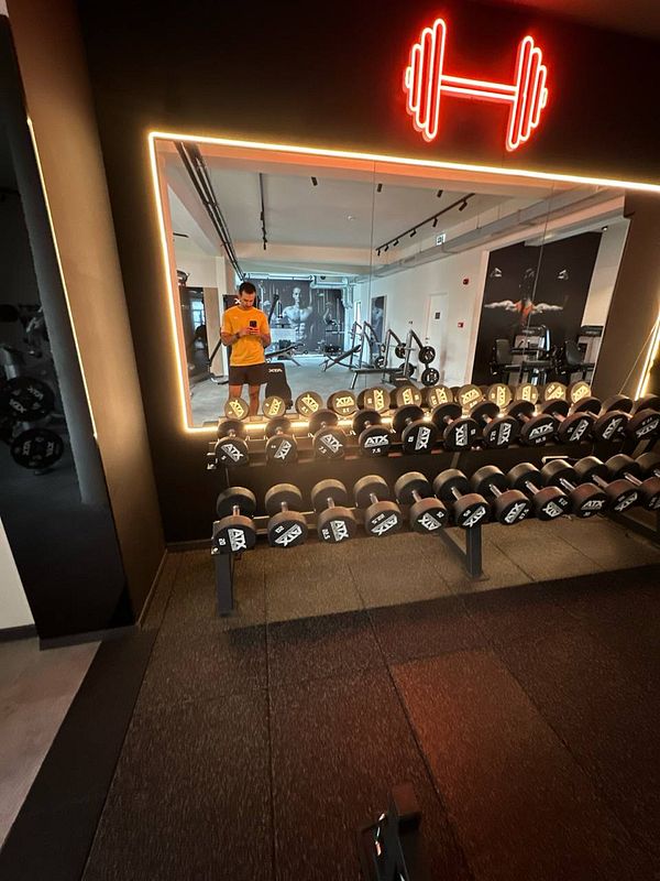 A gym interior featuring a row of dumbbells and a person using a phone.