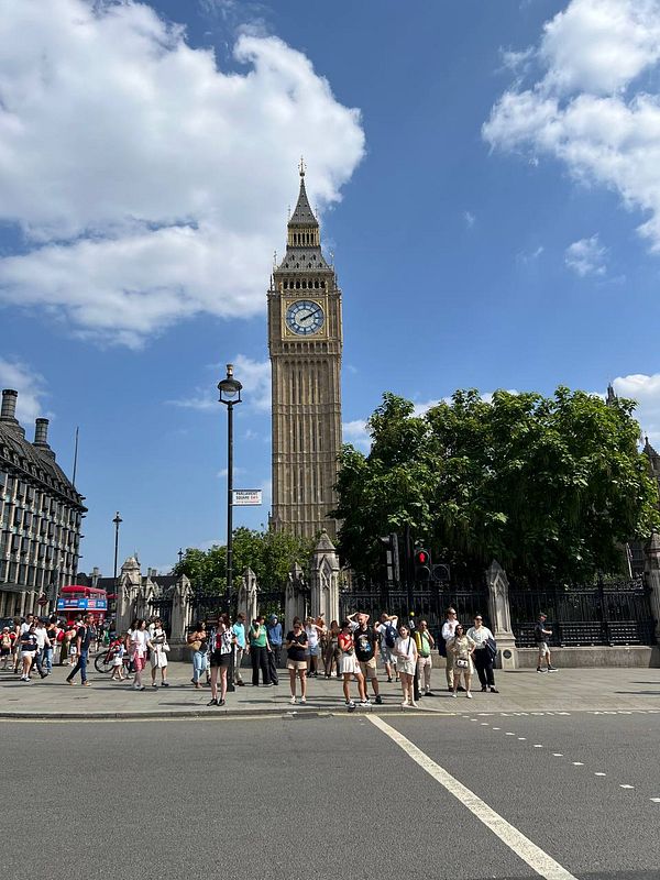 The image captures the iconic Big Ben clock tower in London, surrounded by tourists and a clear blue sky.