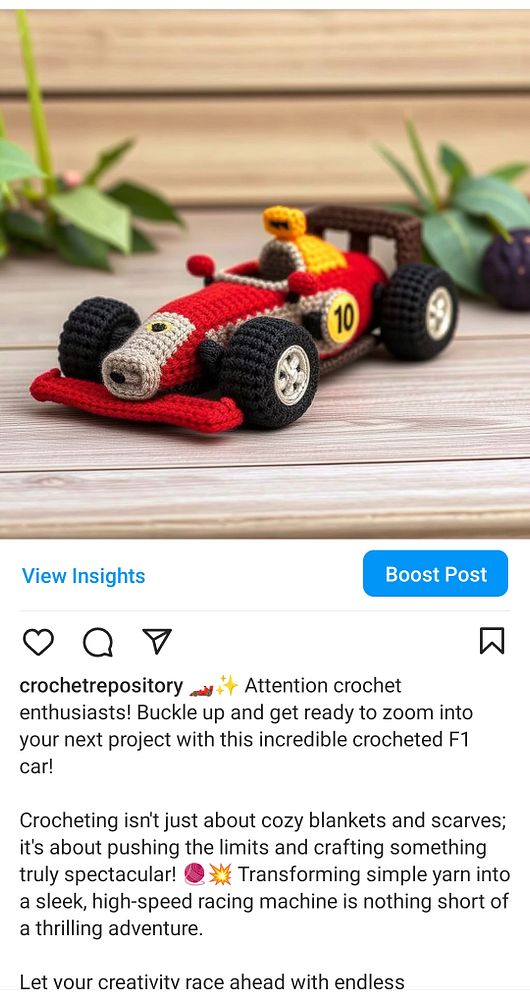 A crocheted model of a Formula 1 car is displayed on a wooden surface with greenery in the background.