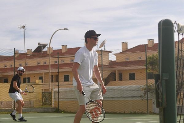 Group of four people enjoying a tennis game on an outdoor court surrounded by green trees and hills.