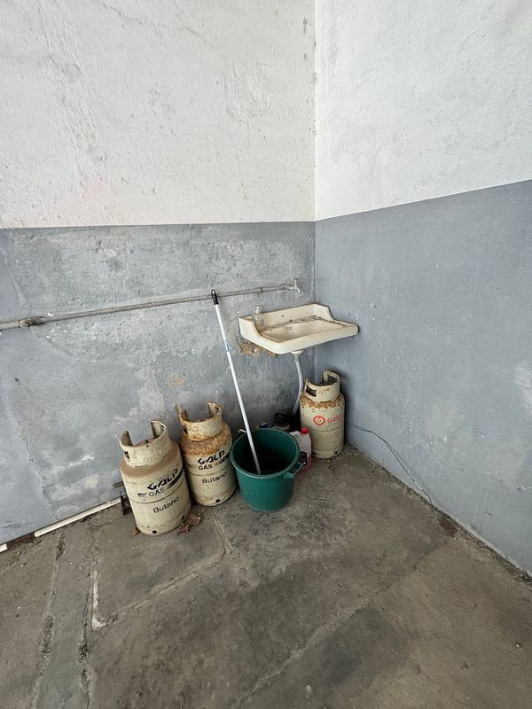 A corner of a room featuring a sink, a mop, a bucket, and several gas canisters.