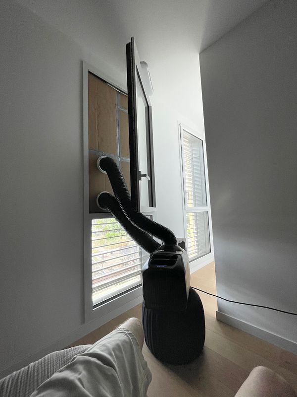 A compact indoor window air conditioner unit installed in a custom window adapter with aluminum foil insulation nearby.