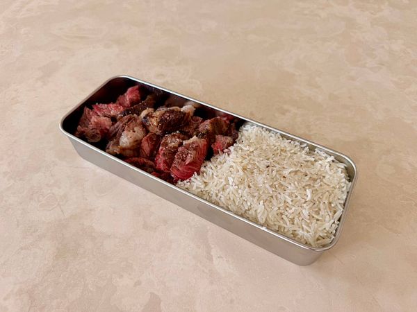 A meal tray with steak, rice, and a side of grapes, prepared for consumption on an airplane.
