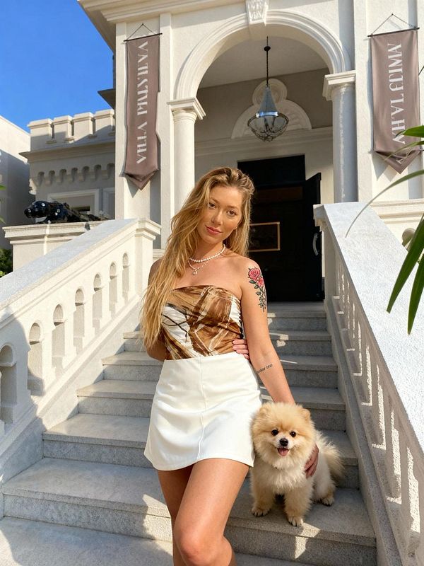 A woman poses on the steps of a grand building with a small fluffy dog.