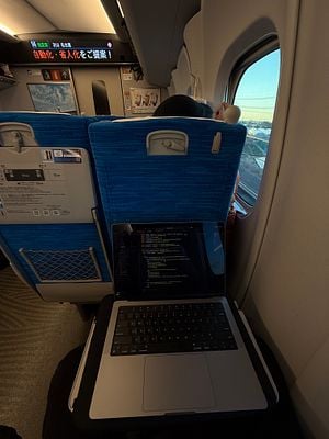 A person is working on a laptop while traveling on a bullet train to Kyoto.