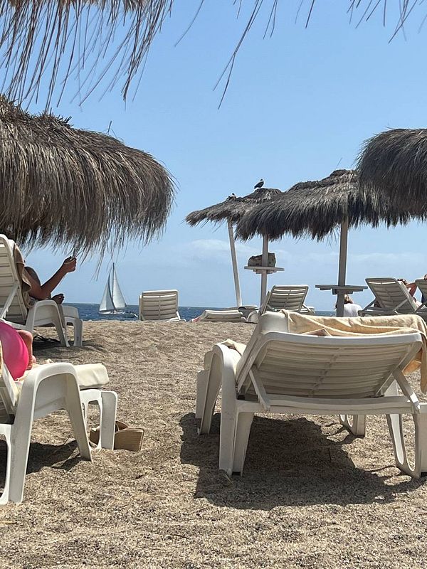 A bright, sunny beach scene with a clear sky, turquoise water, and white sand with people enjoying the beach.
