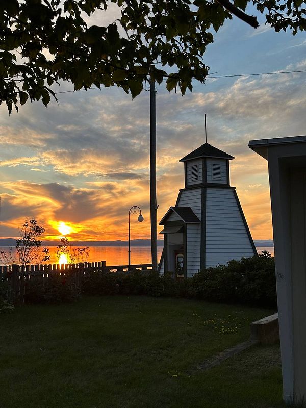 A picturesque sunset over a lake, framed by a charming lighthouse and lush greenery.