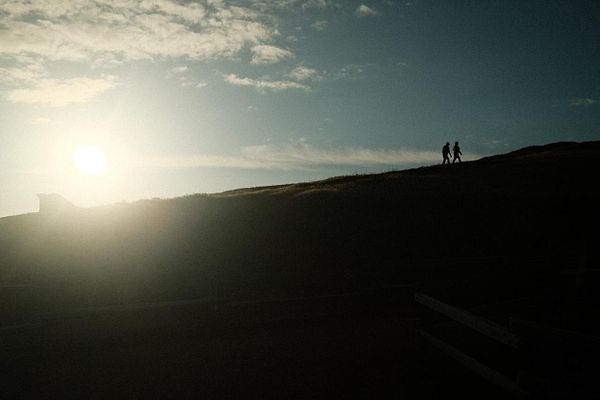 A hiking trail in San Francisco with walkers beside a steep rock face and the city skyline in the distance under a partly cloudy sky.