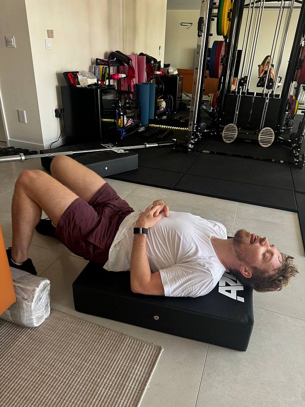 A man is lying on a black exercise mat in a home gym setting.